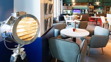 Ein modernes Interieur mit einem runden Spiegel, grau gepolsterten Sesseln, einem weißen runden Tisch und einer Bar mit Regalen und einem Fernseher.