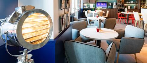 Un interior moderno con un espejo redondo, sillas tapizadas en gris, una mesa redonda blanca y una zona de bar con estanterías y una televisión.