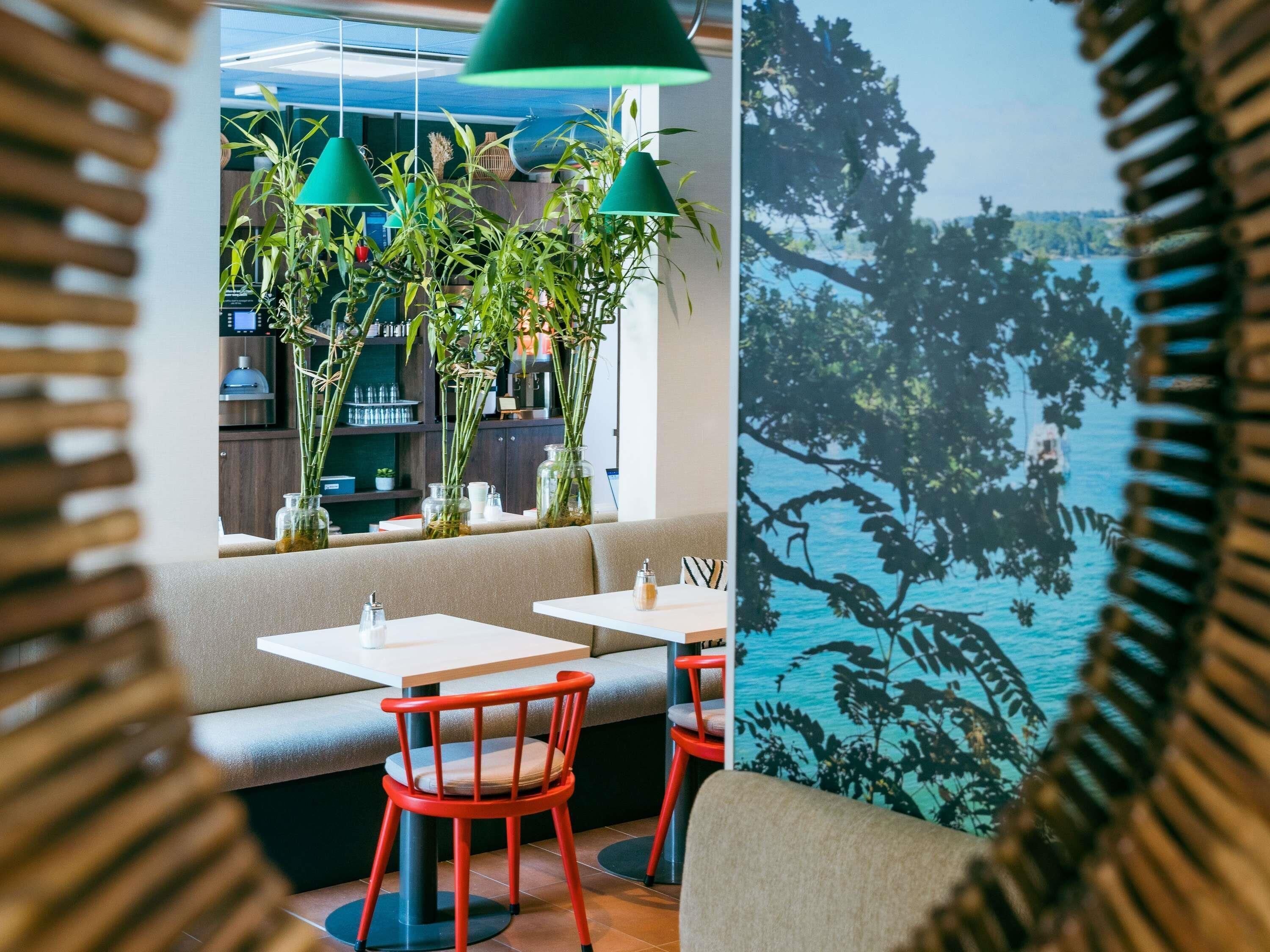 Ein Restaurant mit Blick auf das Wasser, ausgestattet mit grünen Hängeleuchten, roten Stühlen und einer Sitzgelegenheit mit Seeblick.