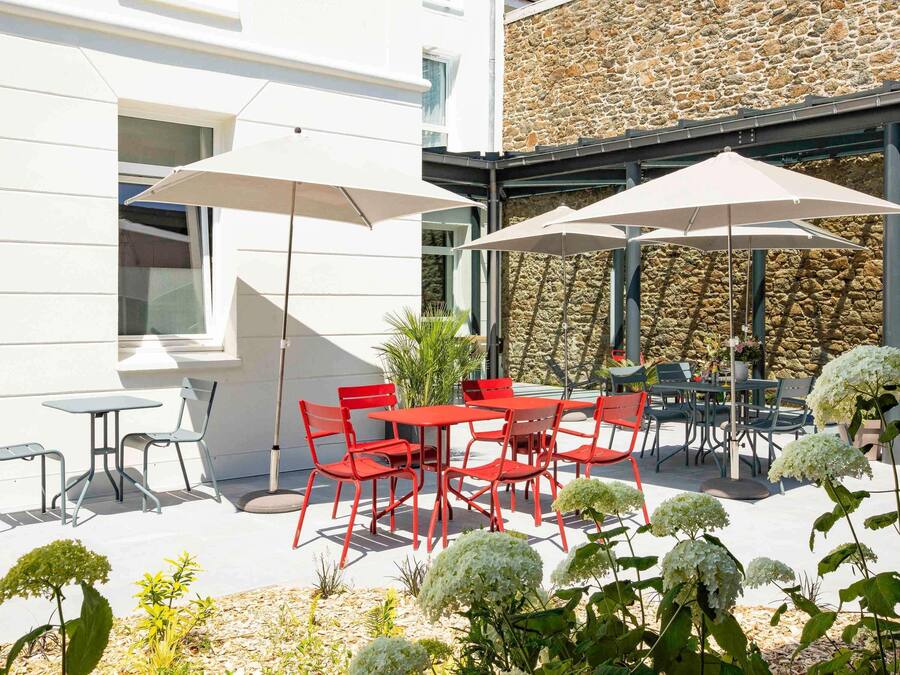 An outdoor patio with red chairs and tables, white umbrellas, and a stone wall.