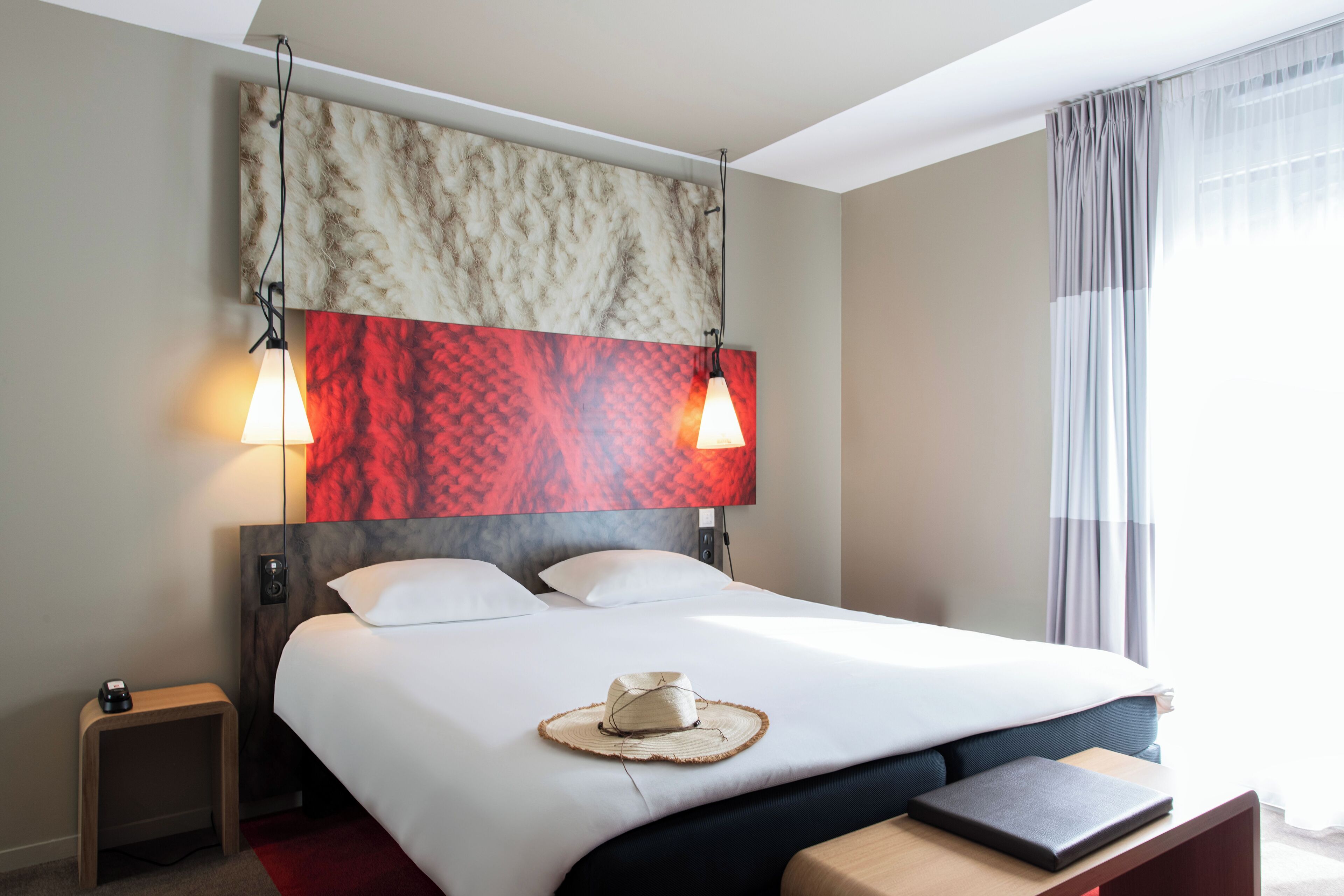 Una habitación de hotel moderna con una cama grande, una mesita de noche, una lámpara y una obra de arte en la pared.