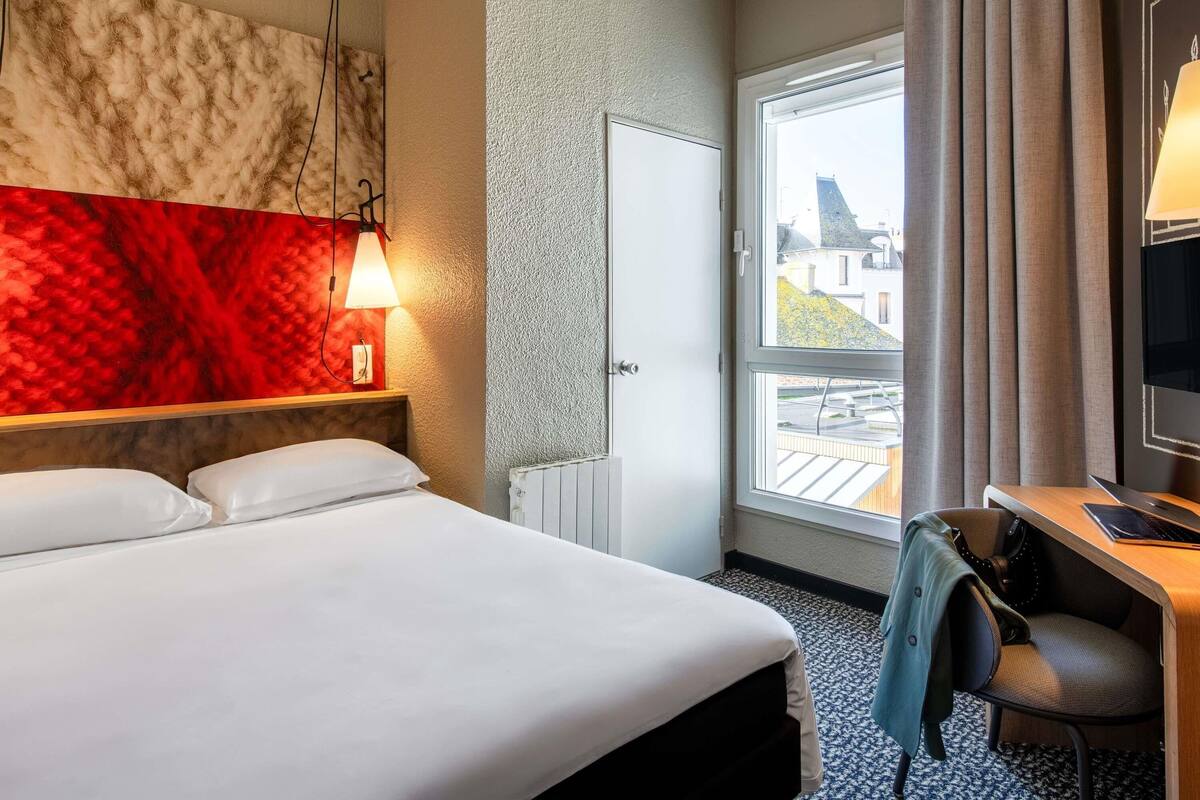 Une chambre d’hôtel comprenant un lit, un bureau avec une chaise, une télévision, une fenêtre donnant sur un paysage agréable et une lampe.