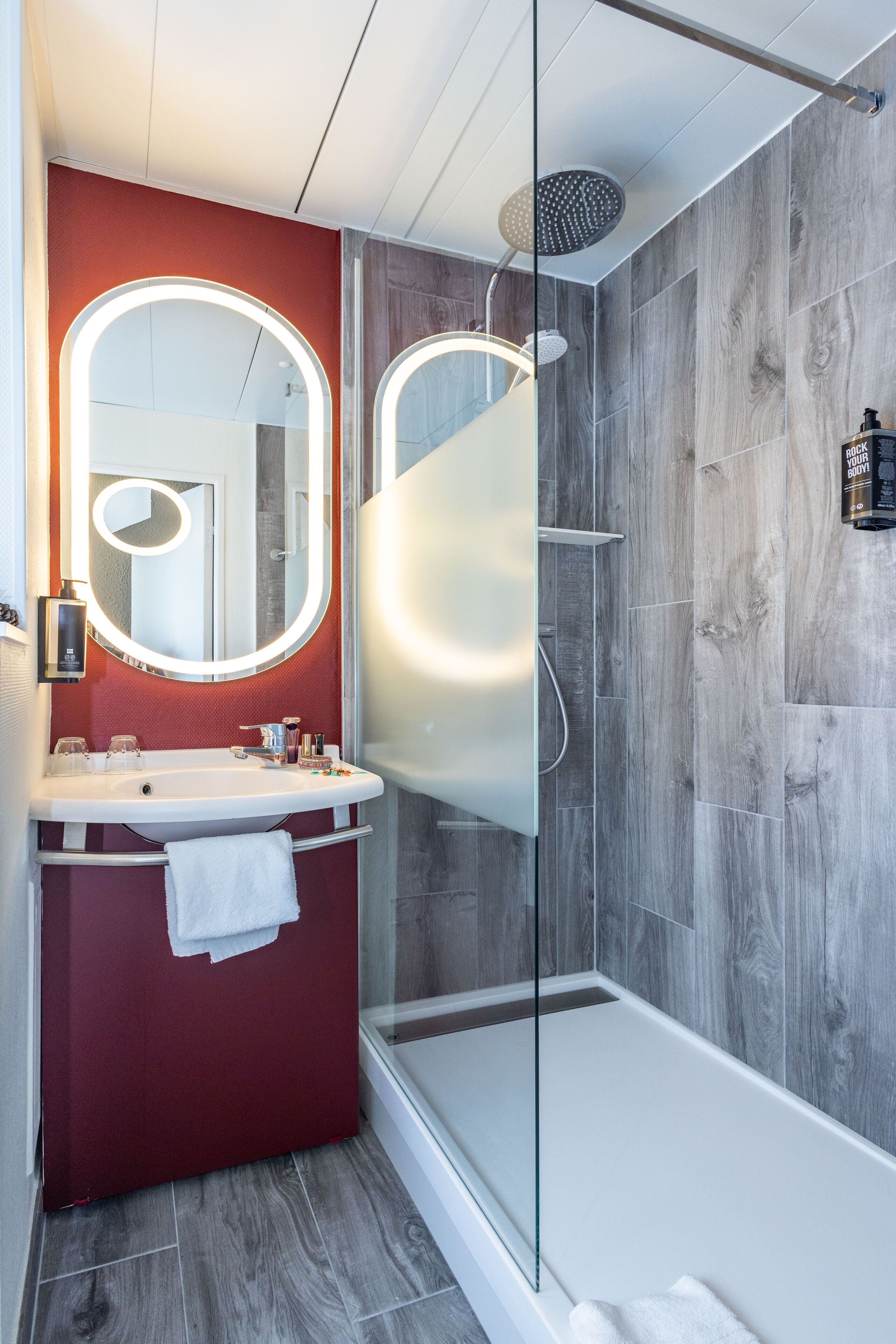 A modern bathroom with a glass-enclosed shower, a vanity with a mirror, and a red accent wall.