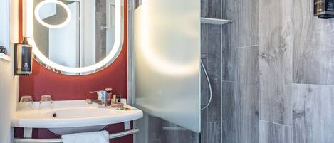 A modern bathroom with a glass-enclosed shower, a vanity with a mirror, and a red accent wall.