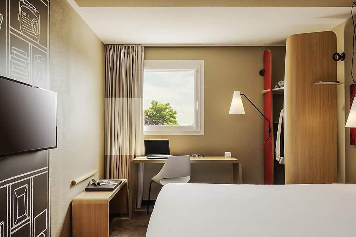 A hotel room with a bed, desk, chair, TV, and a window with curtains.