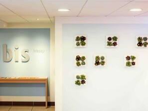 A reception area with a light blue wall, a wooden bench, and a wall-mounted display of succulents. - ibis Massy (Massy)