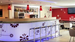 Un área de bar moderna con mostrador, taburetes y pared roja con motivos florales.