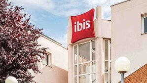 Exterior de un hotel ibis con un llamativo letrero rojo, fachada de ladrillo y un área de entrada bien cuidada.