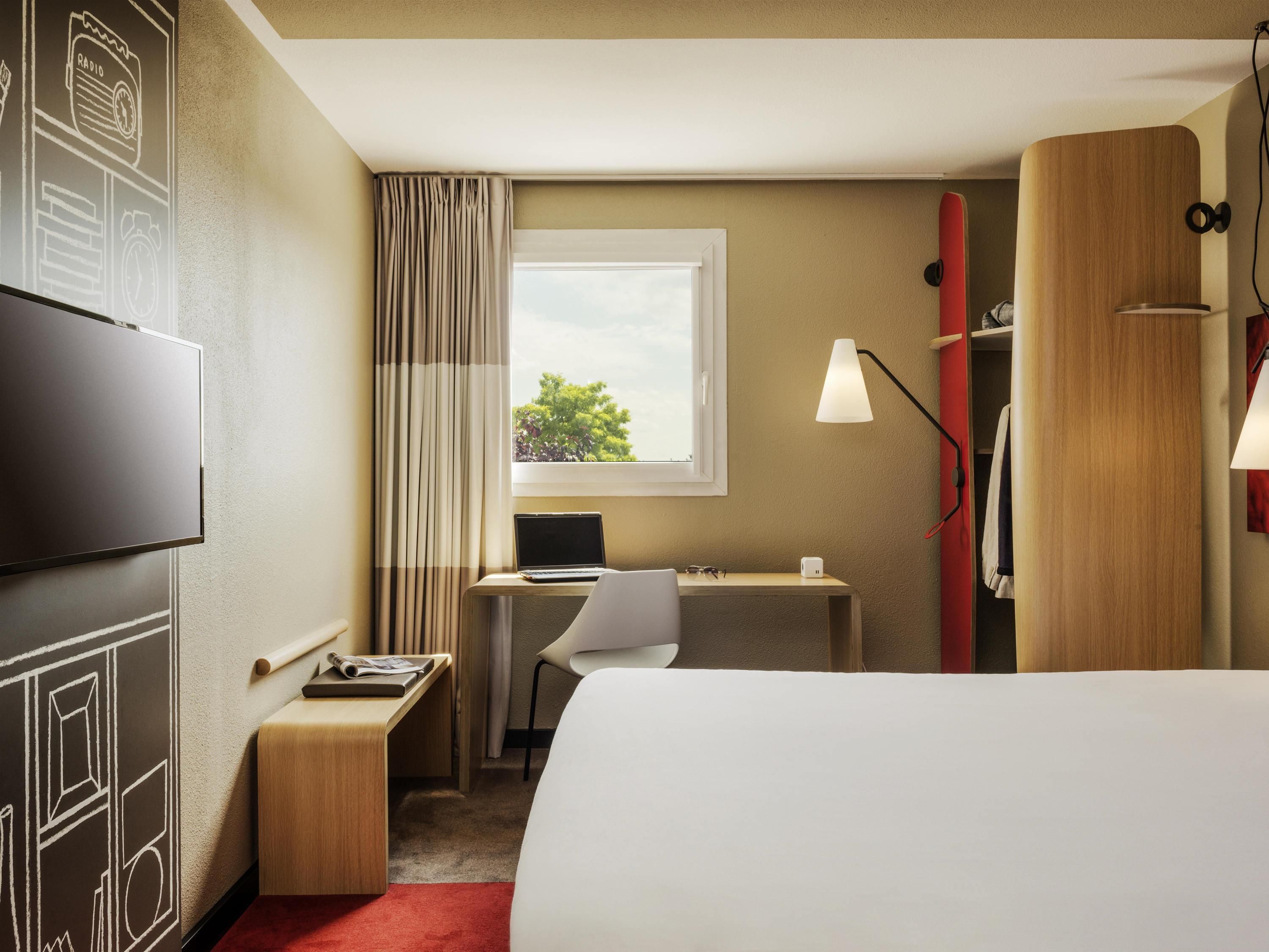 A hotel room with a bed, desk, chair, TV, and a window with curtains.