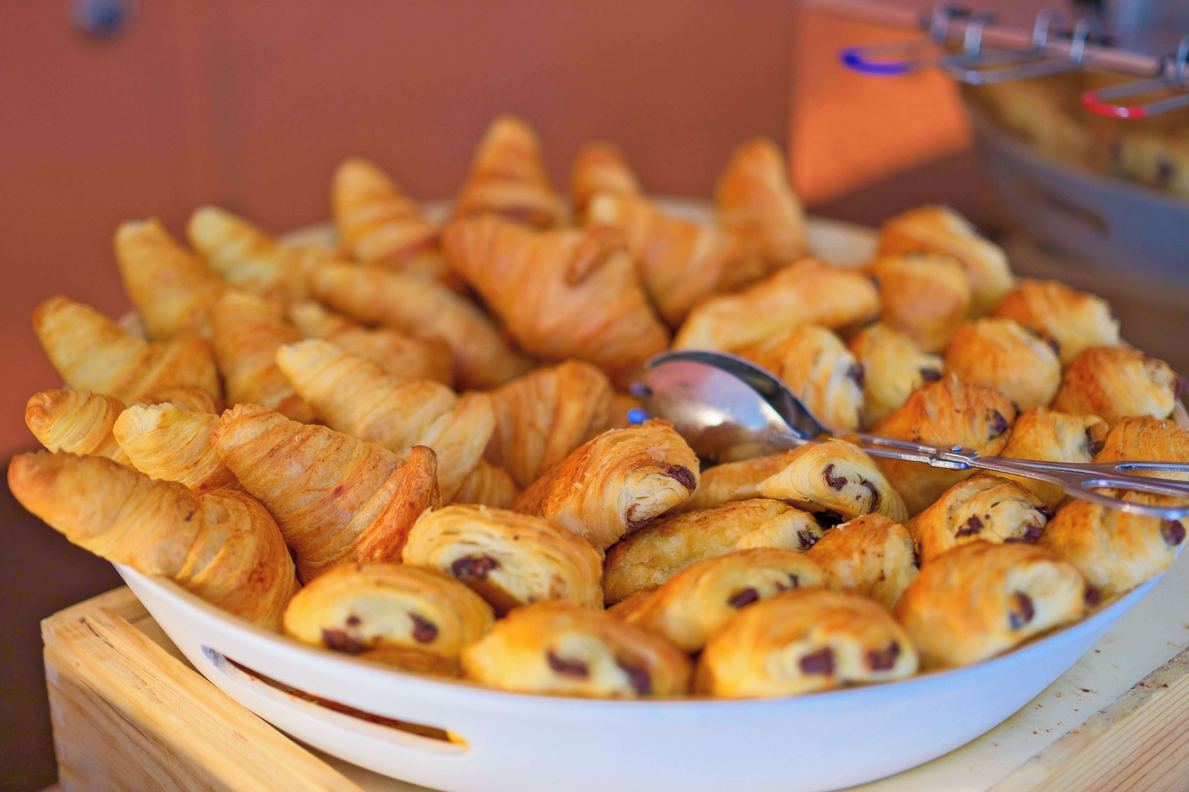 A bowl of assorted pastries, including croissants and chocolate-filled pastries, on a wooden surface.