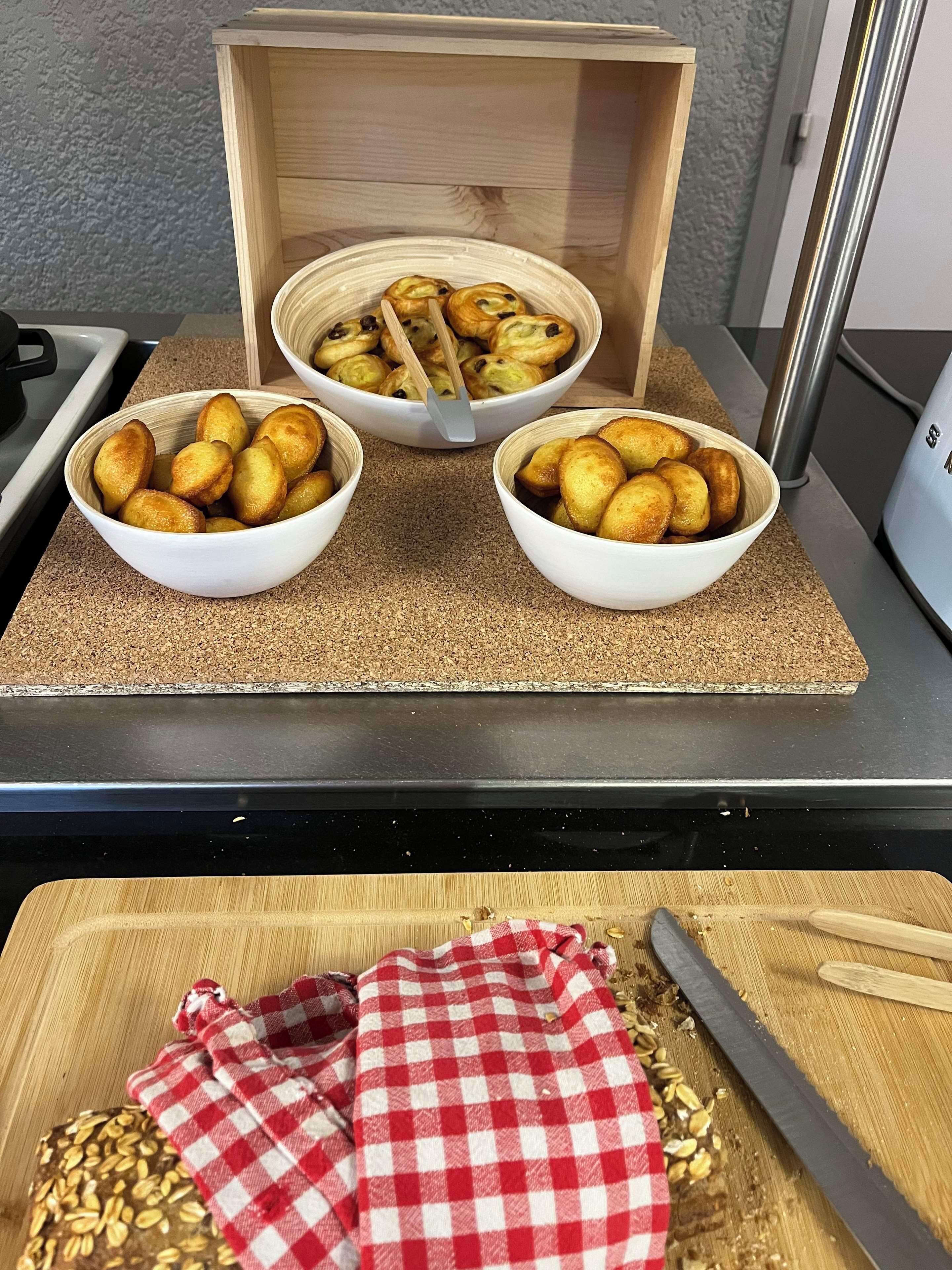 Three bowls of golden-brown pastries on a kitchen counter with a cutting board and a checkered cloth nearby.