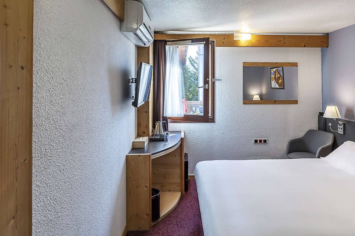 Hotellihuone, jossa on sänky, työpöytä tuolilla, televisio ja ikkuna, jossa on verhot.