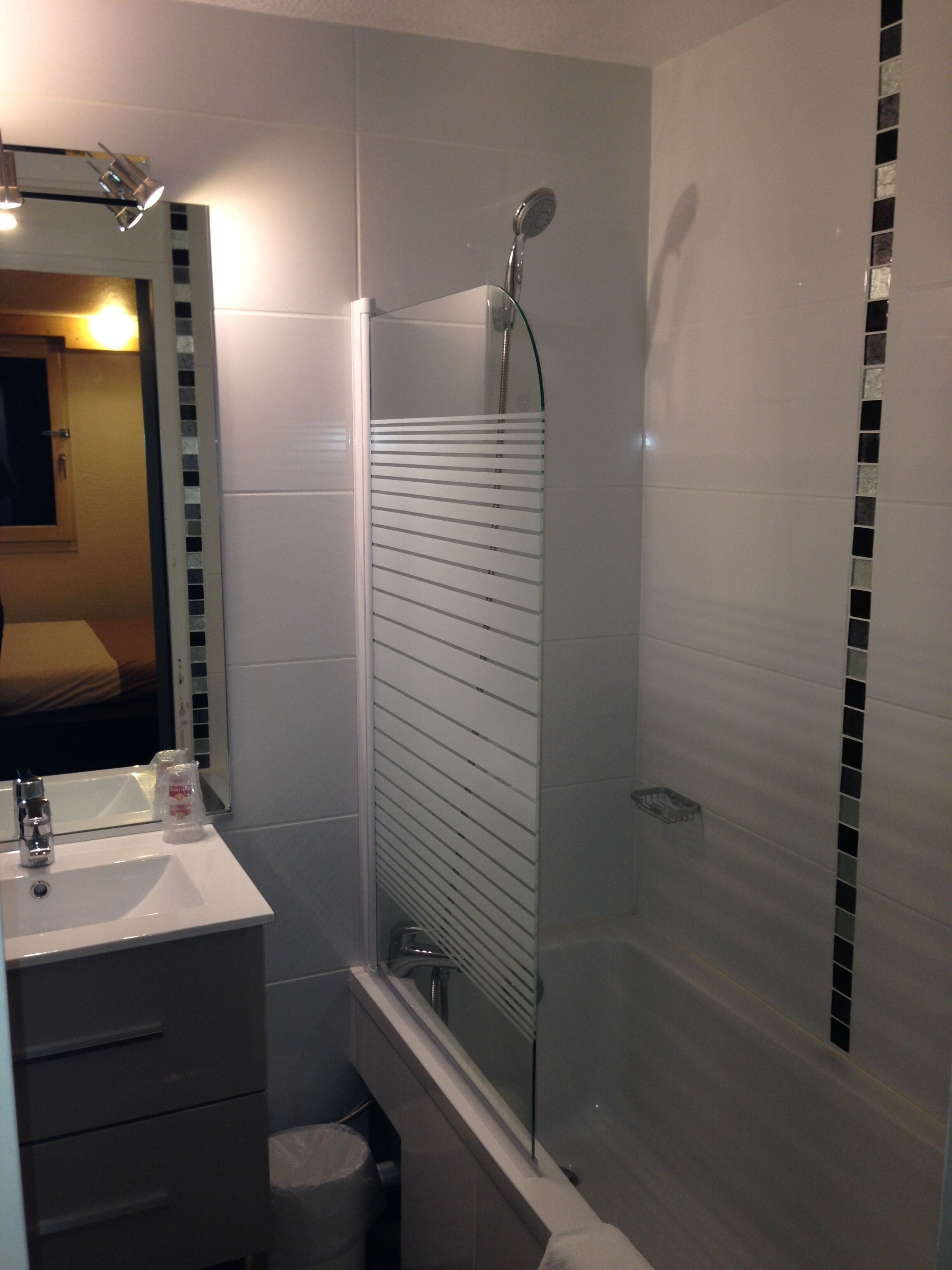 A modern bathroom with a glass shower enclosure, a white sink, and a mirror above the sink.