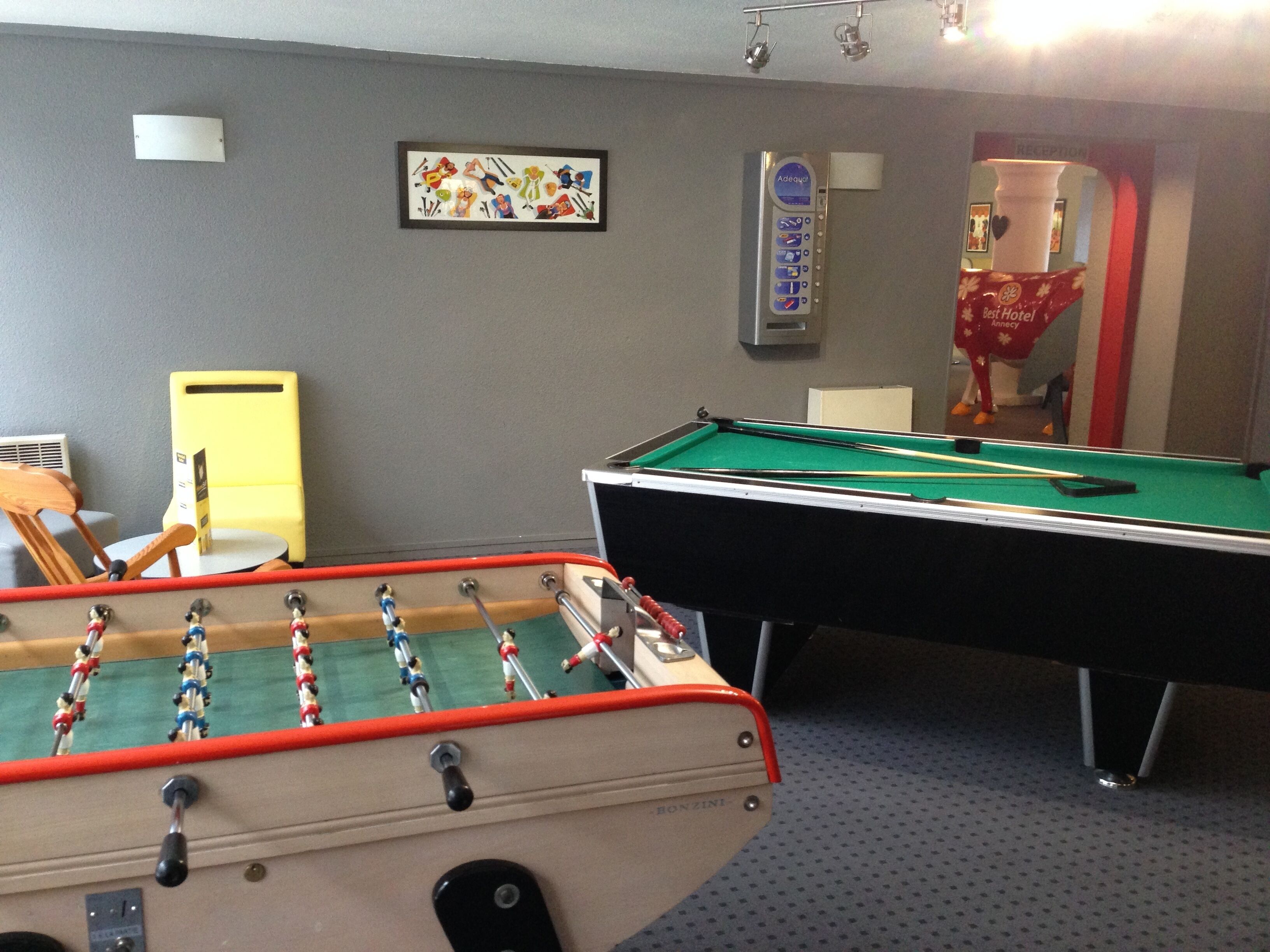A room with a foosball table, a pool table, and a reception area with a sign.