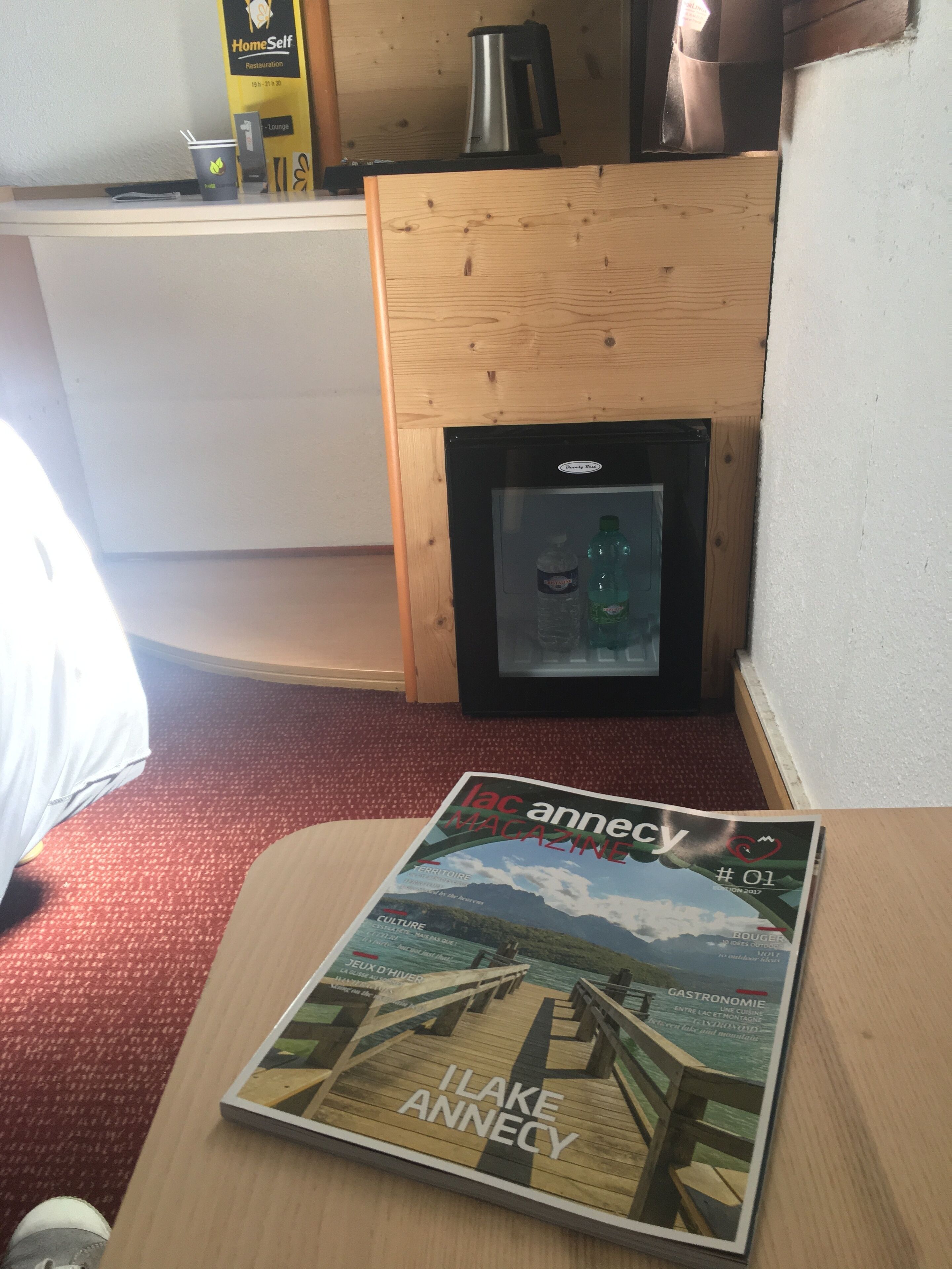 A magazine on a table, a refrigerator, and a coffee machine in a room.