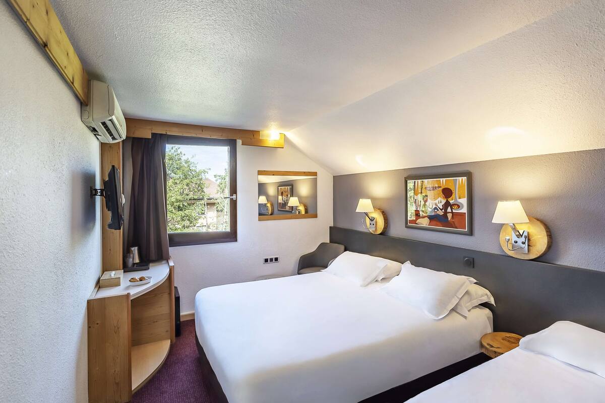 Hotellihuone, jossa on sänky, yöpöytä, lamppu ja ikkuna, jossa on verhot.