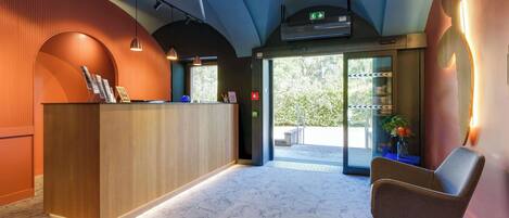 A reception area with a wooden reception desk, a modern chair, and a glass door leading outside.