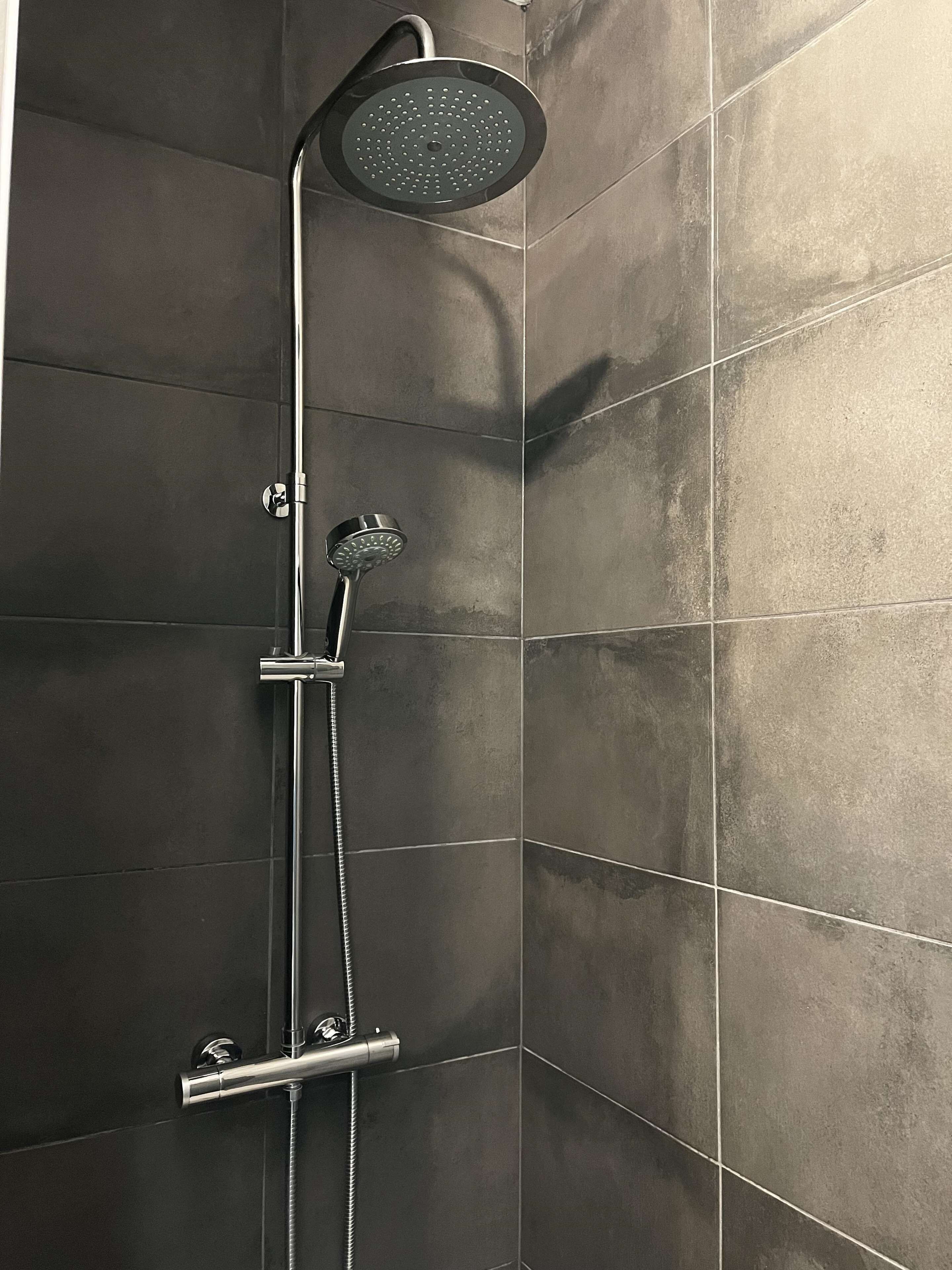 A shower with a handheld showerhead and a wall-mounted control valve.