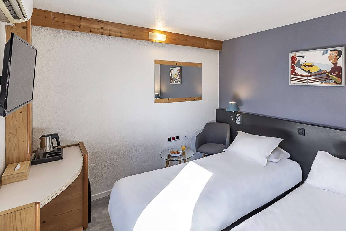Hotellihuone, jossa on kaksi sänkyä, työpöytä, televisio ja taideteoksia seinillä.