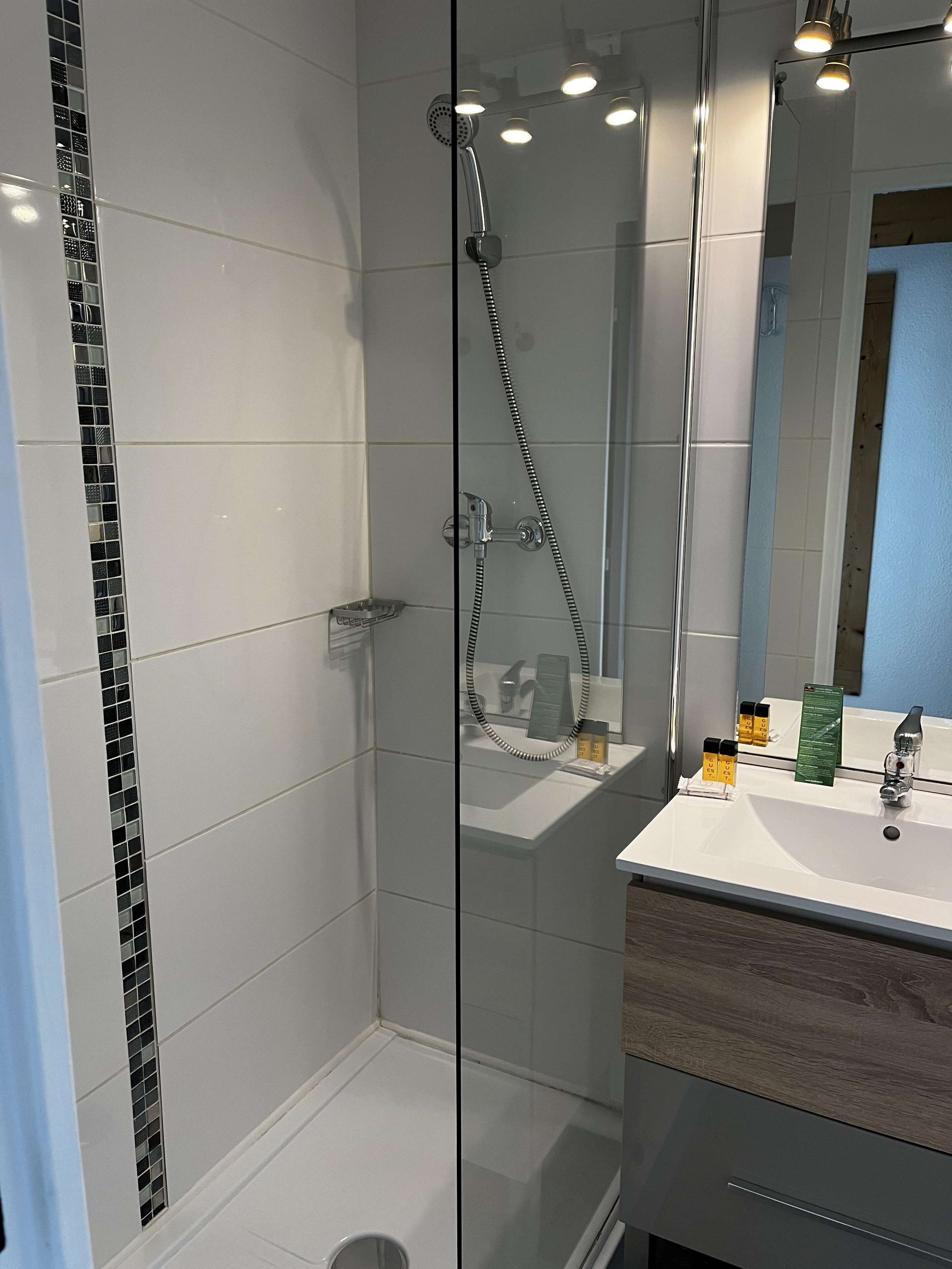 Un baño moderno con ducha envuelta en vidrio, un lavamanos blanco con encimera de madera y un espejo sobre el lavamanos.