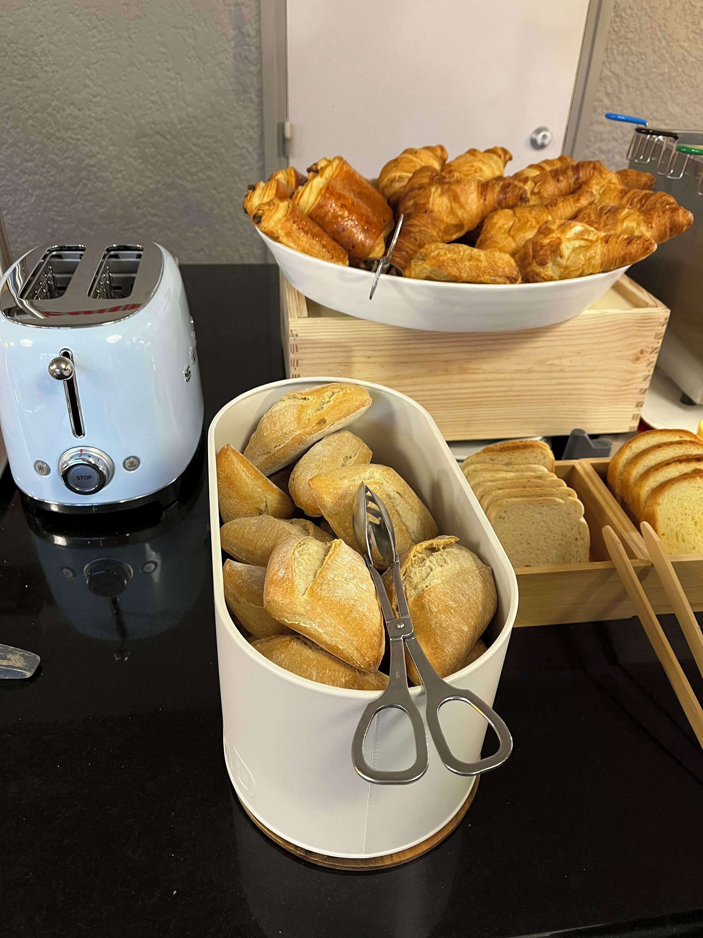 A kitchen counter with a toaster, a bowl of croissants, a bowl of breadsticks, and a pair of scissors.