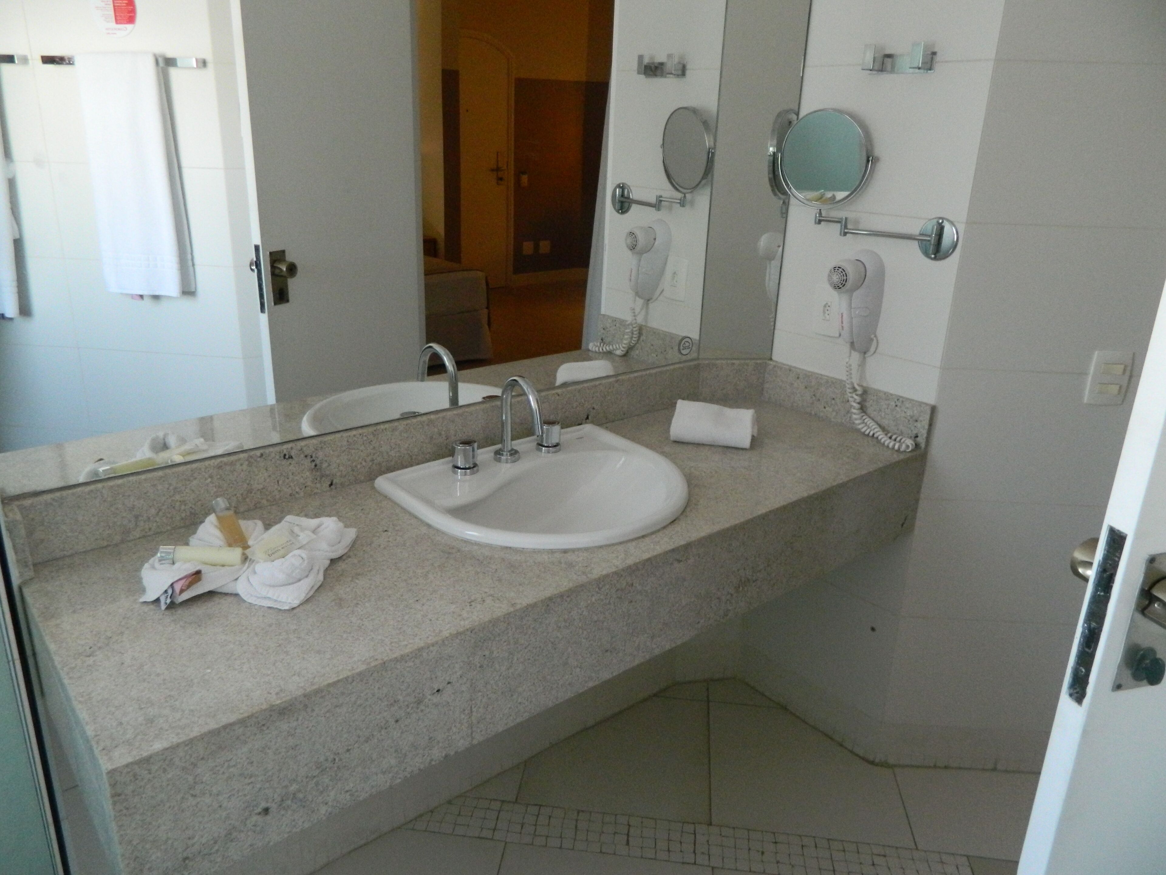 Un baño con lavamanos, dos espejos, una toalla y un secador de pelo.