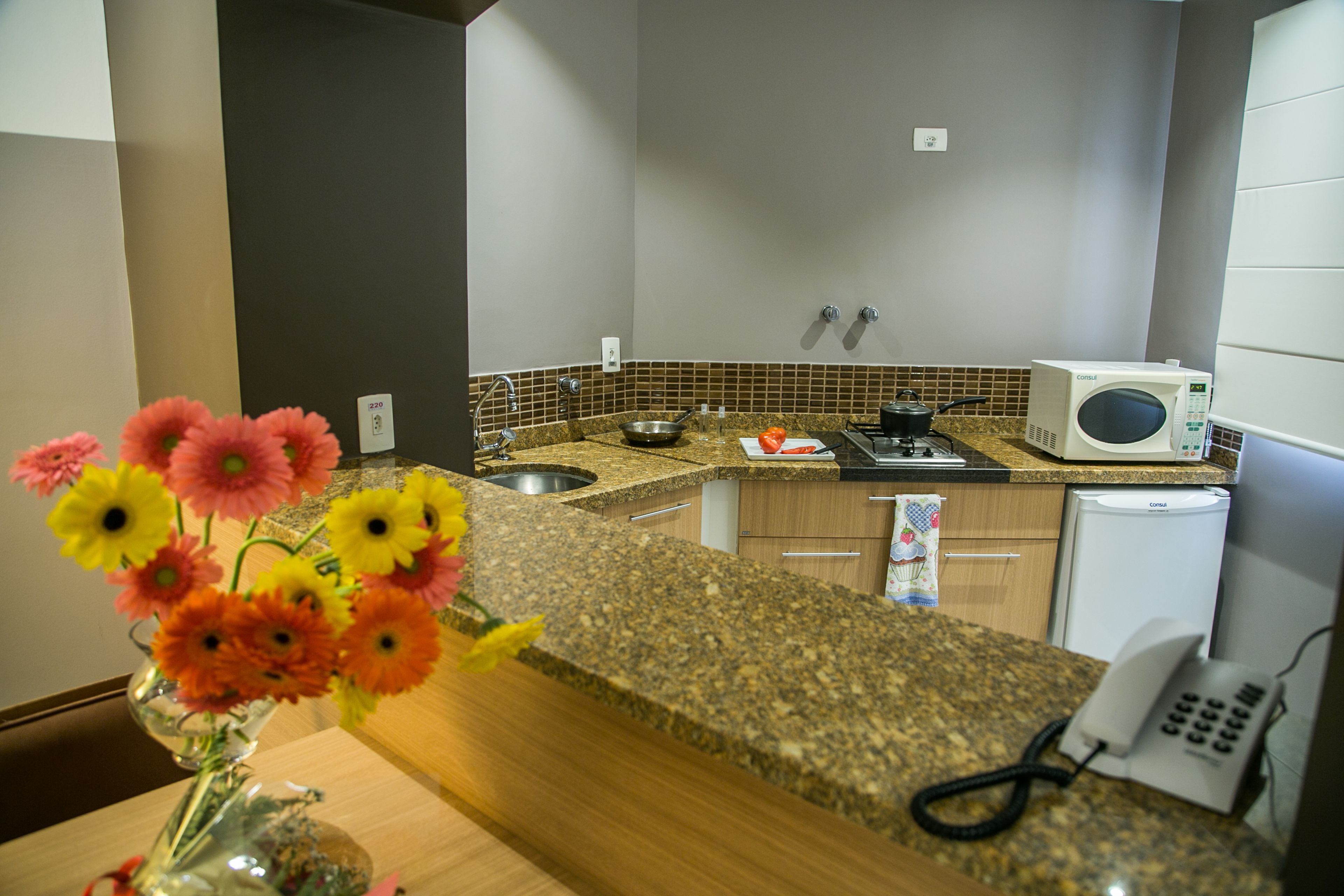 A kitchen with granite countertops, a microwave, a sink, and a telephone.