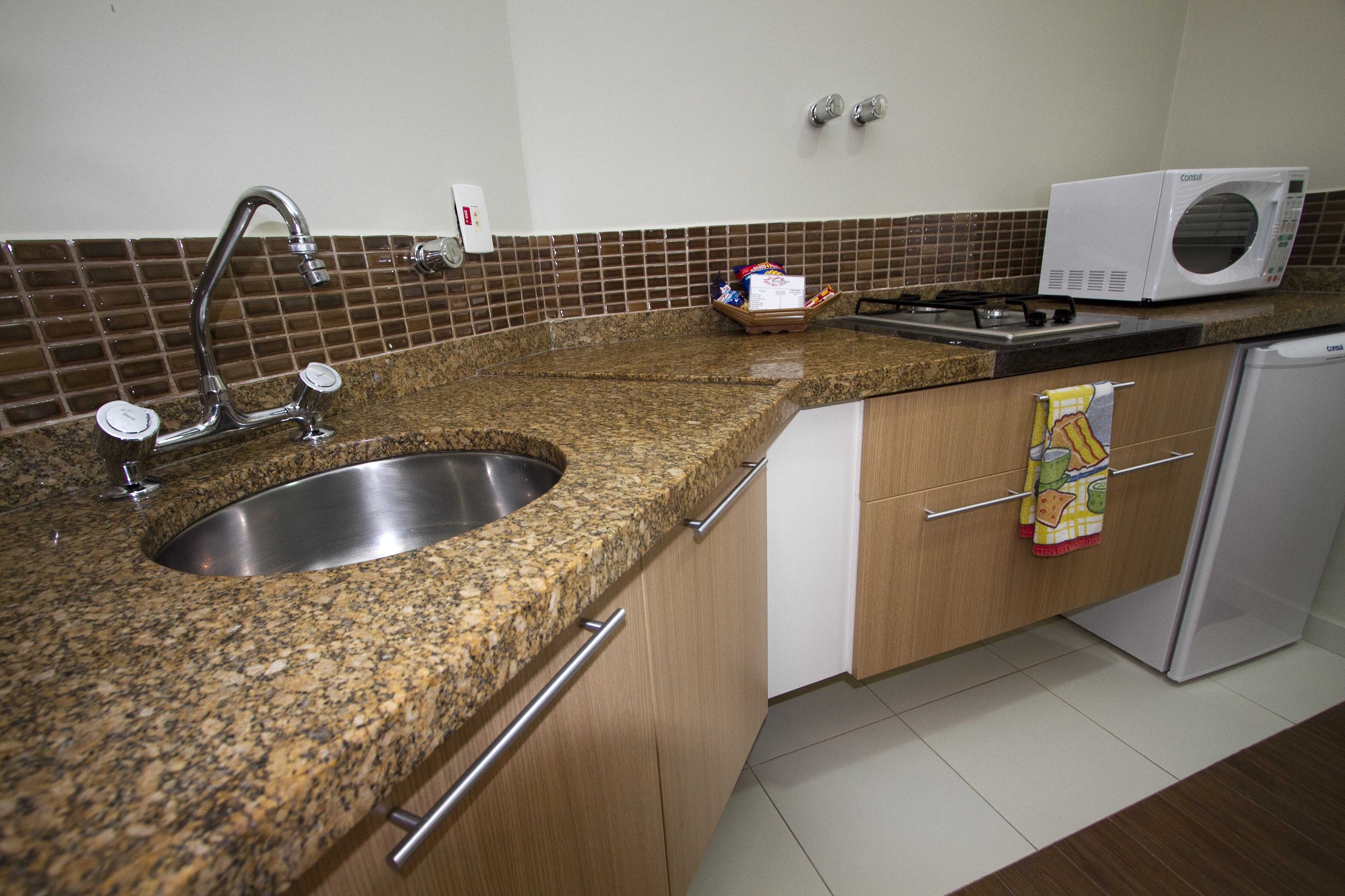A kitchen with a granite countertop, stainless steel sink, a microwave, and a small refrigerator.