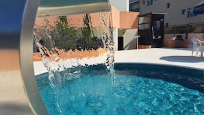 Ein Schwimmbecken mit klarem Wasser, einer Metallkonstruktion und einem Gebäude im Hintergrund.