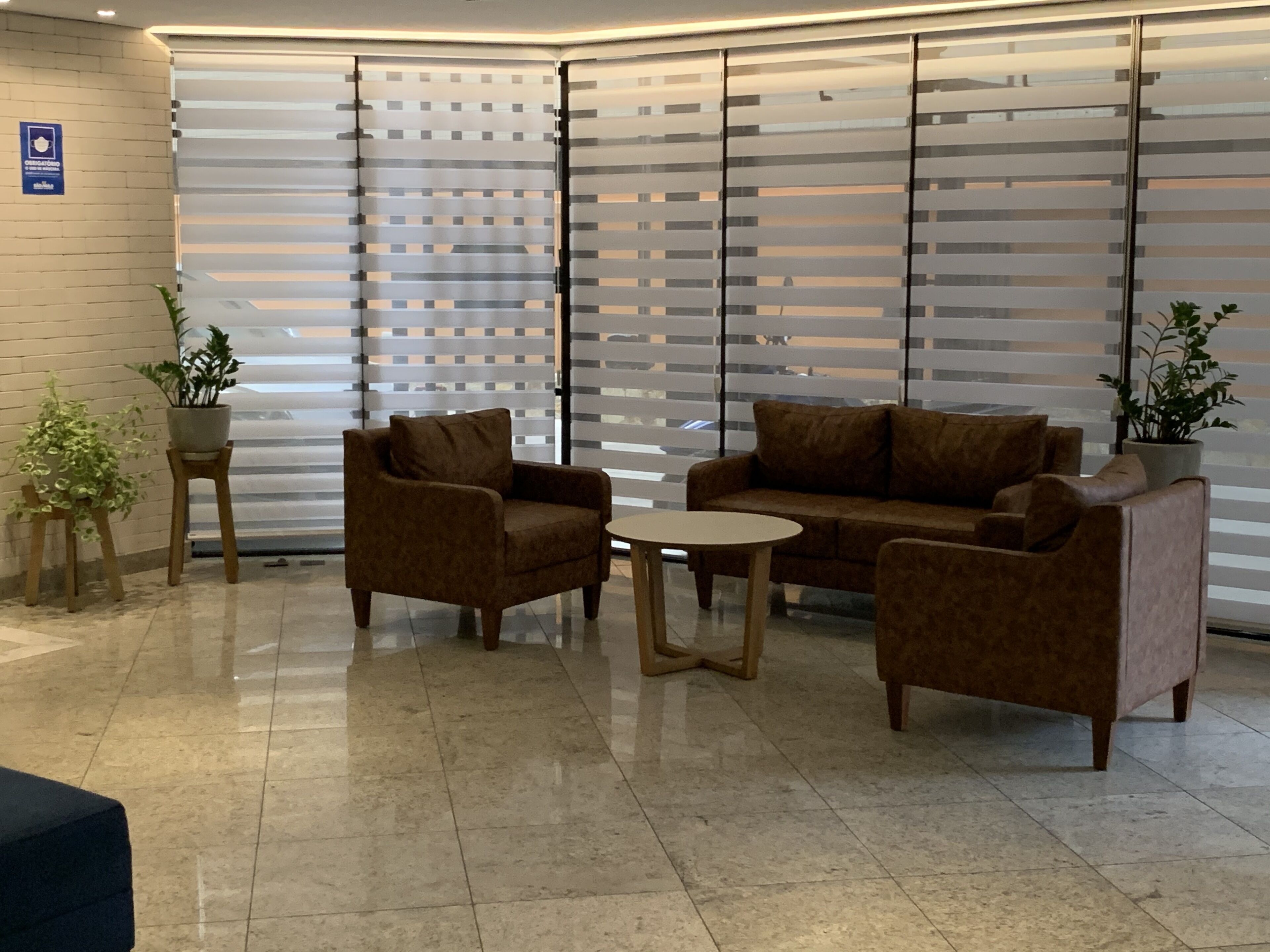 A modern waiting area with two sofas and a small table, a potted plant, and a sign on the wall.