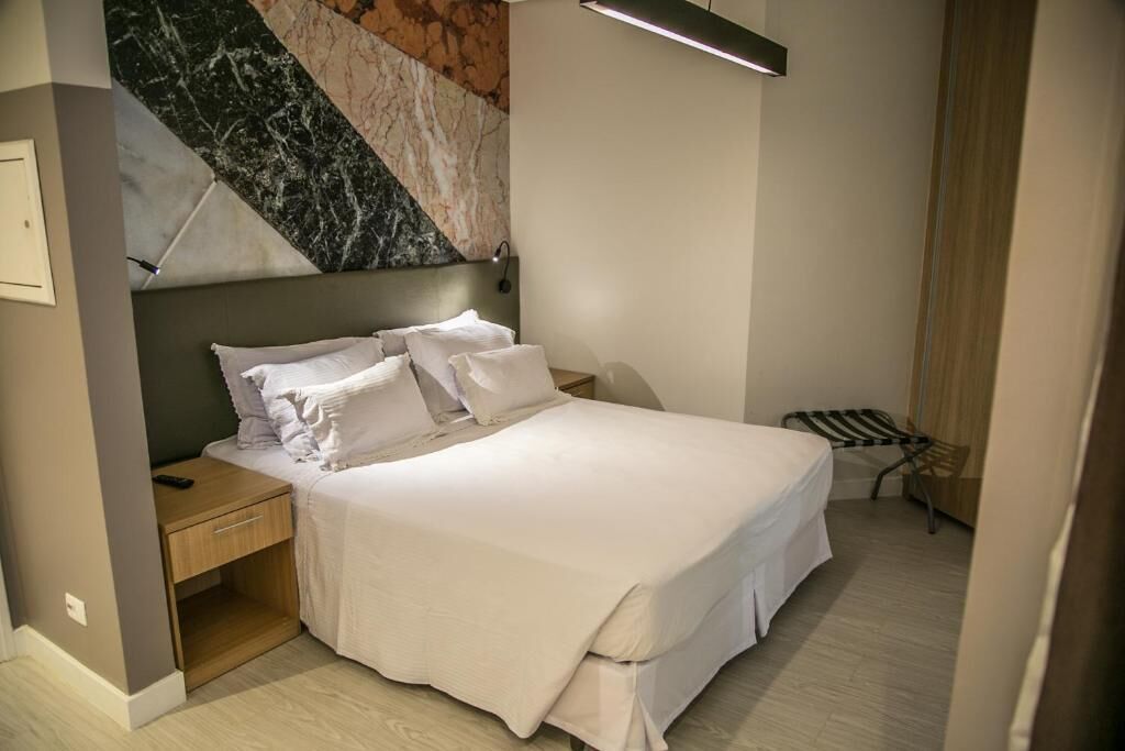 A modern bedroom with a large bed, a nightstand, a wall-mounted lamp, and a striped chair.