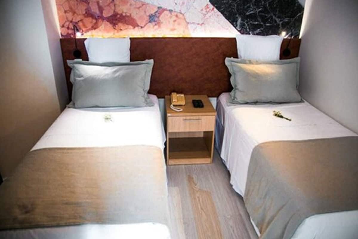 A hotel room with two single beds, a wooden nightstand with a telephone, and a marble-patterned wall.