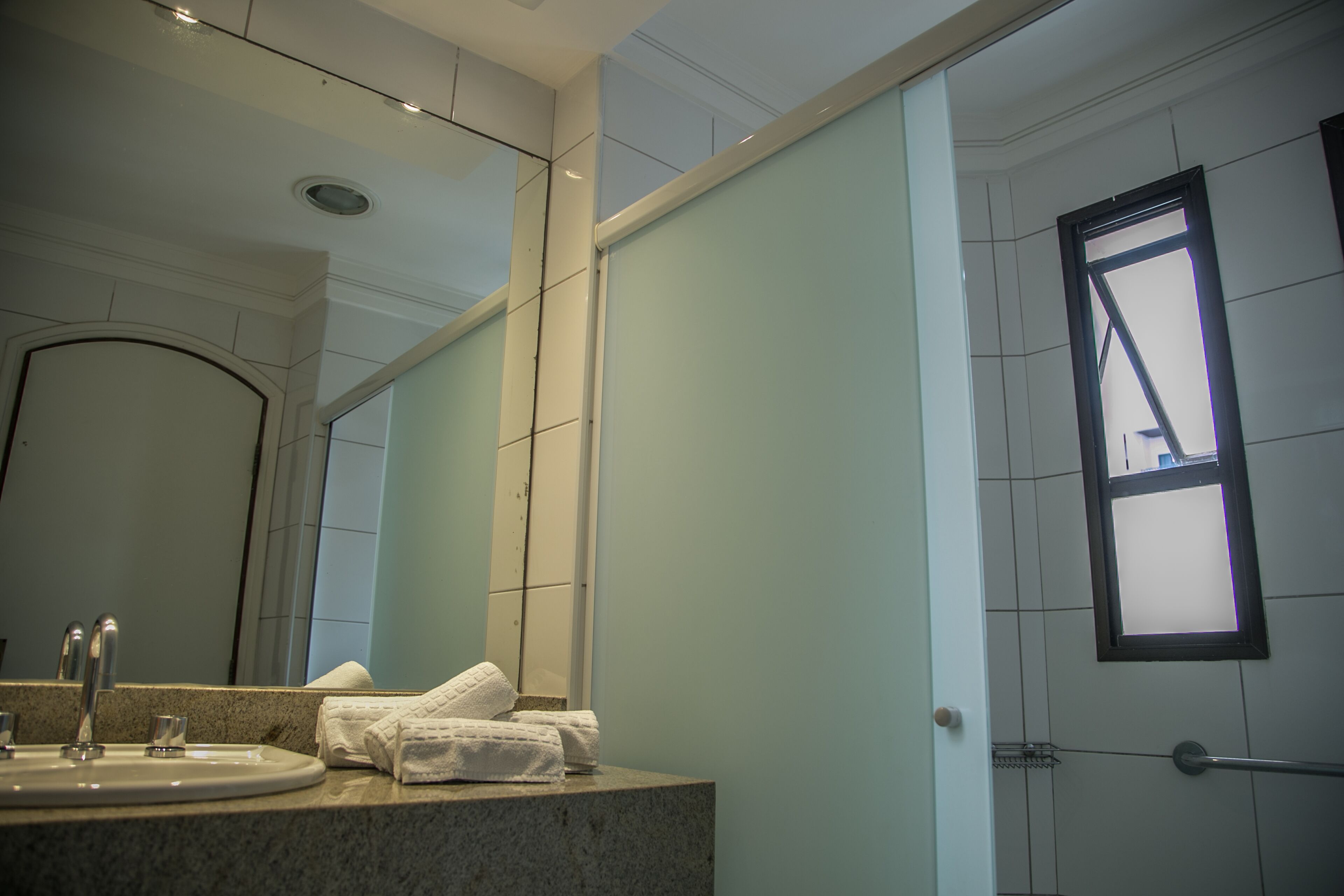 Un baño con lavamanos, espejo, toallas y ventana.