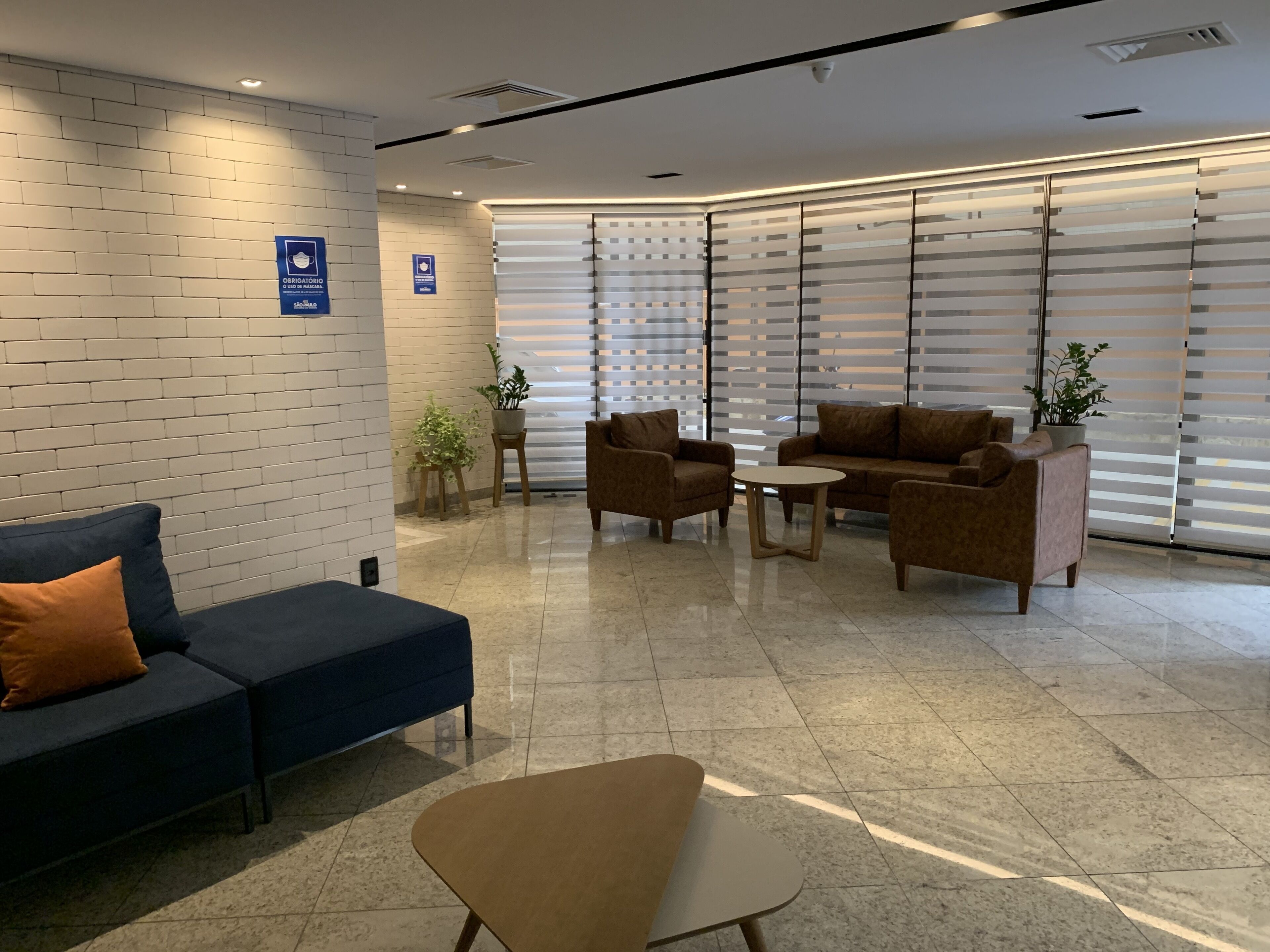 Un área de espera moderna con un sofá azul, un sillón marrón y una pequeña mesa redonda.