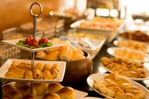 A buffet with various food items including pastries, bread, and a salad with a decorative stand. - My Place Savassi Hotel Boutique (Belo Horizonte)
