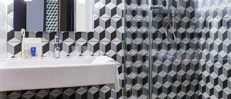 Un baño con pared de diseño geométrico, un lavabo con artículos de aseo personal y una mampara de ducha de vidrio.