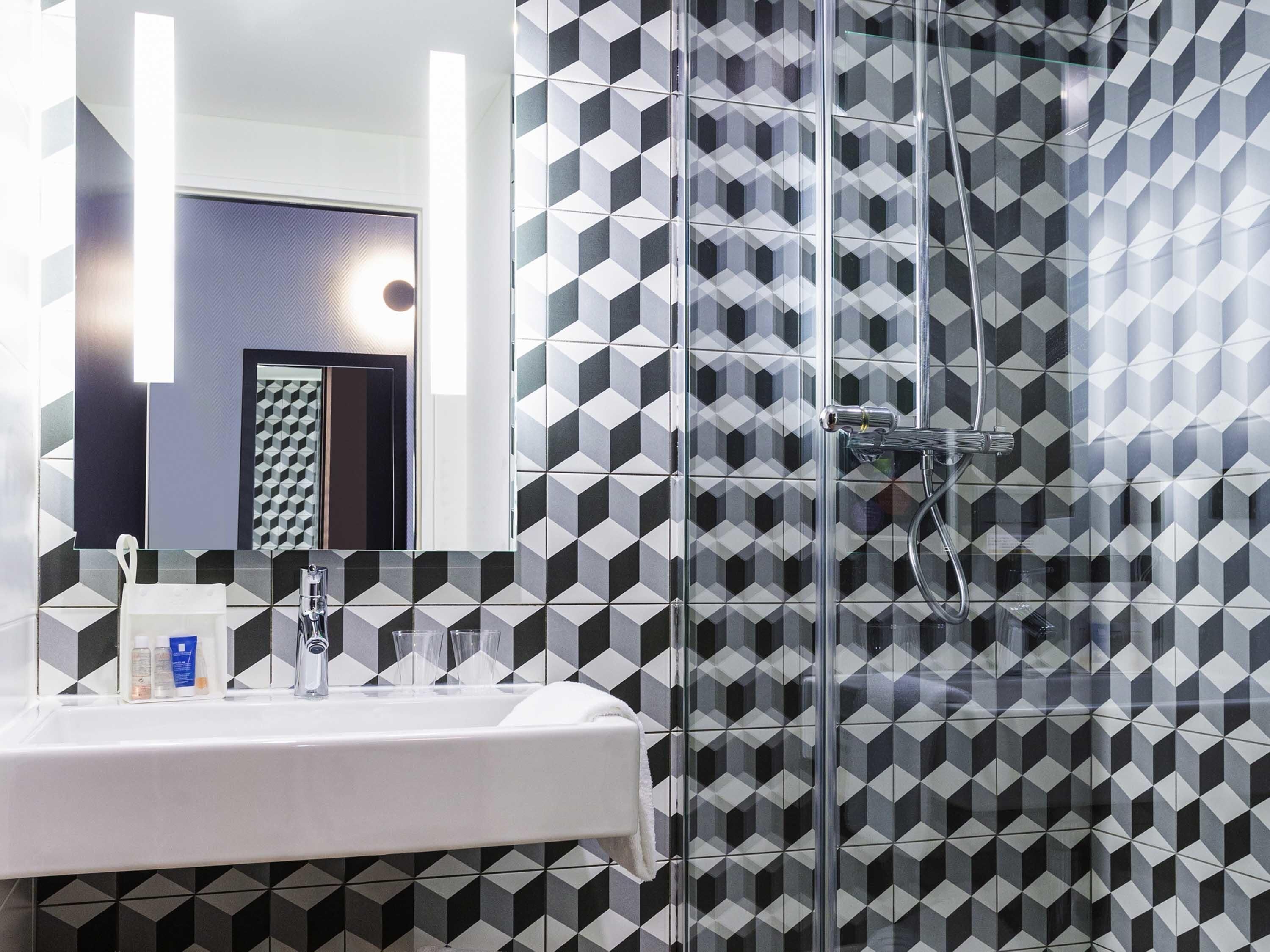 A modern bathroom with a geometric tile backsplash, a white sink, and a glass shower enclosure.