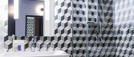 A modern bathroom with a geometric tile backsplash, a white sink, and a glass shower enclosure.