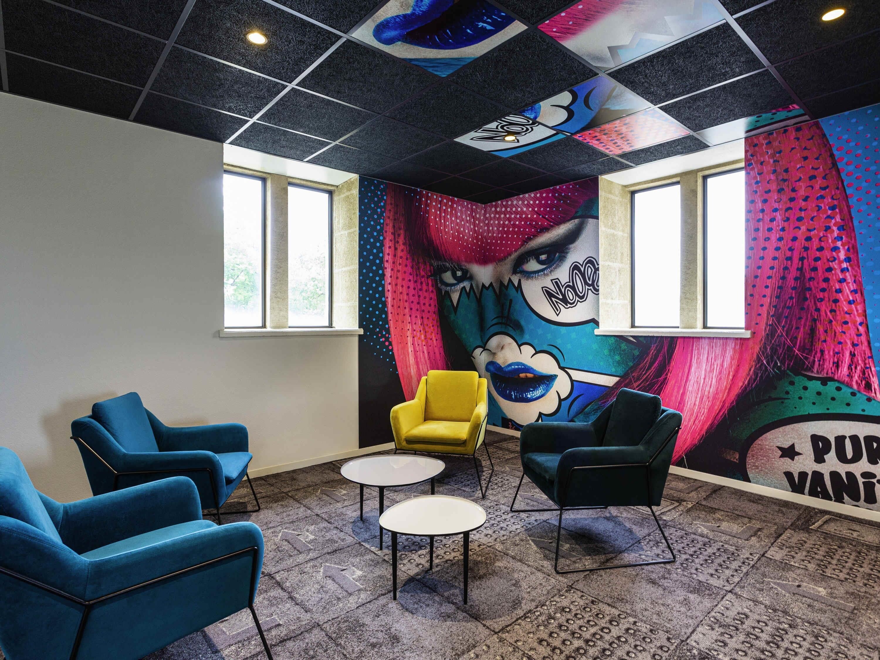 Una habitación con un mural llamativo, sillas azules y negras, una silla amarilla y una mesita blanca.