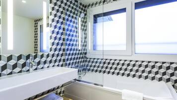 Un baño moderno con un diseño geométrico en los azulejos, un espejo grande, una bañera y una ventana que ofrece vistas.