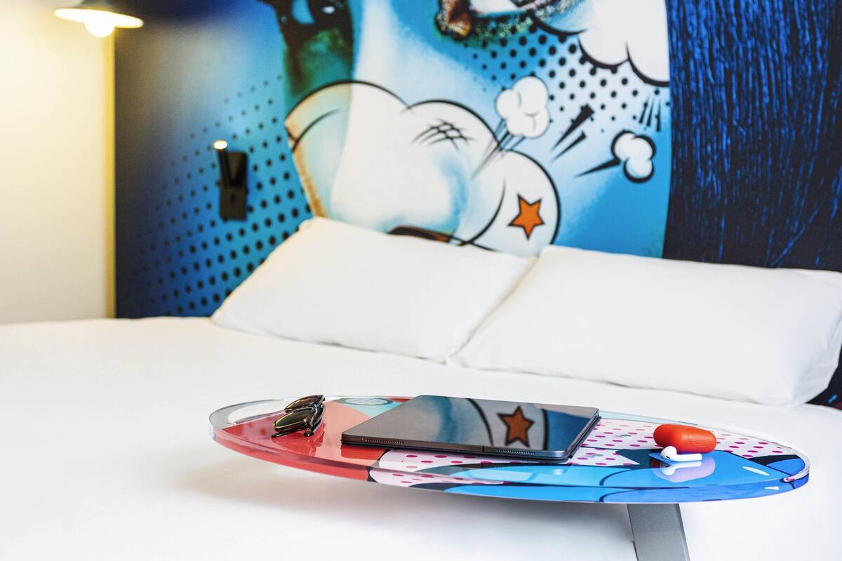 Een bed met een wit kussen en kleurrijke muurdecoratie met een stripfiguur.