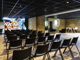 Un salón de conferencias con filas de sillas, una pantalla grande mostrando un gráfico, paredes de piedra y una mesa de billar.