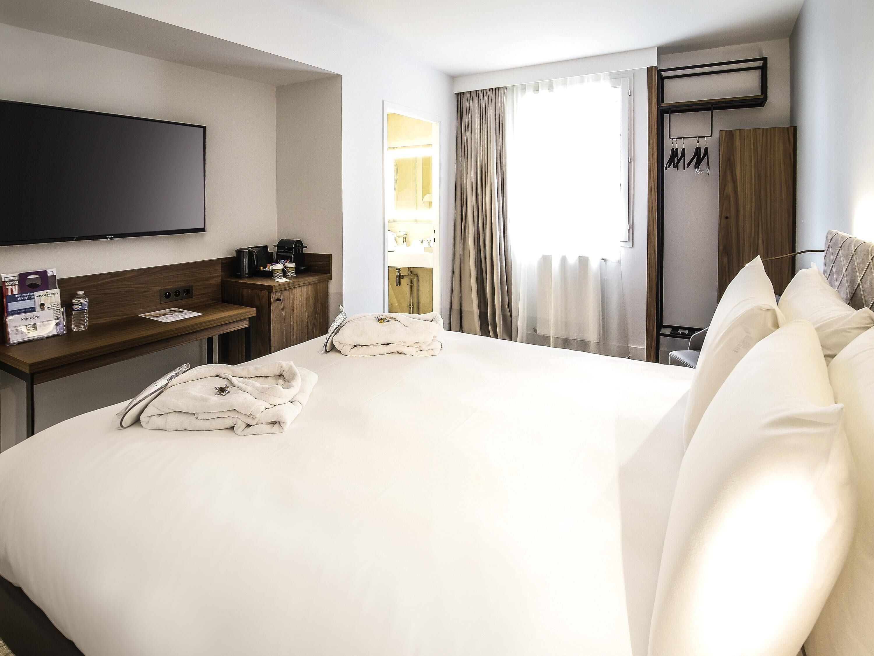 A hotel room with a large bed, a flat-screen TV, a desk with a coffee maker, and a shower area.