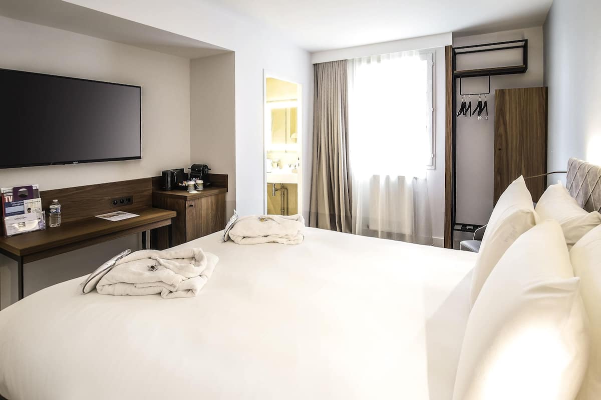 A hotel room with a large bed, a flat-screen TV, a desk with a coffee maker, and a shower area.