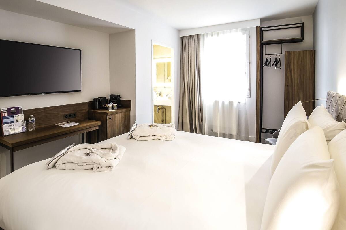 A hotel room with a large bed, a flat-screen TV, a desk with a coffee maker, and a shower area.