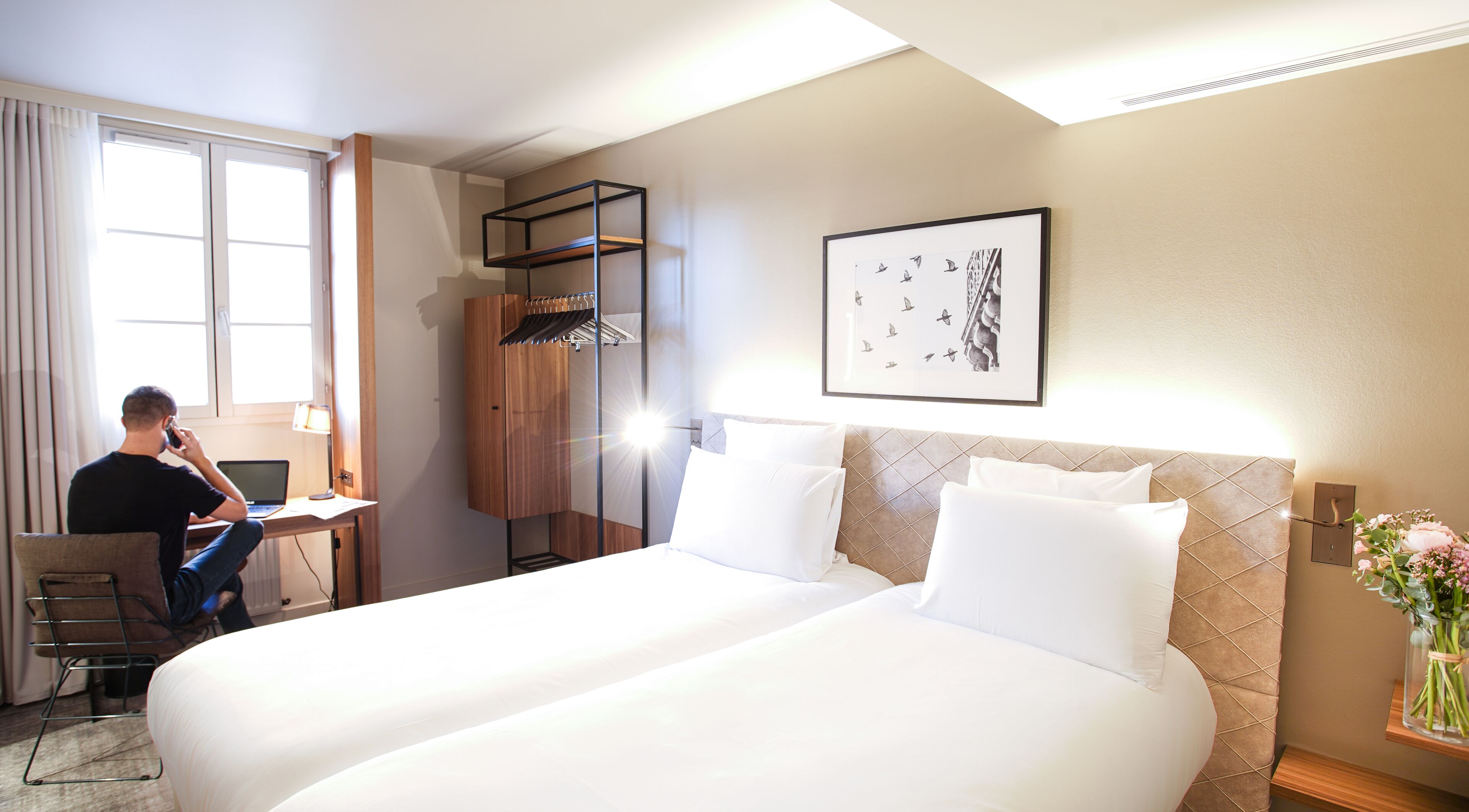 Una habitación de hotel con dos camas, un escritorio con una computadora portátil, una silla y un armario.