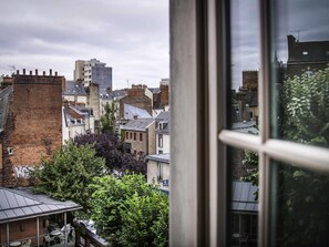 A view through a window of a cityscape with various buildings, including a brick structure and a modern high-rise.