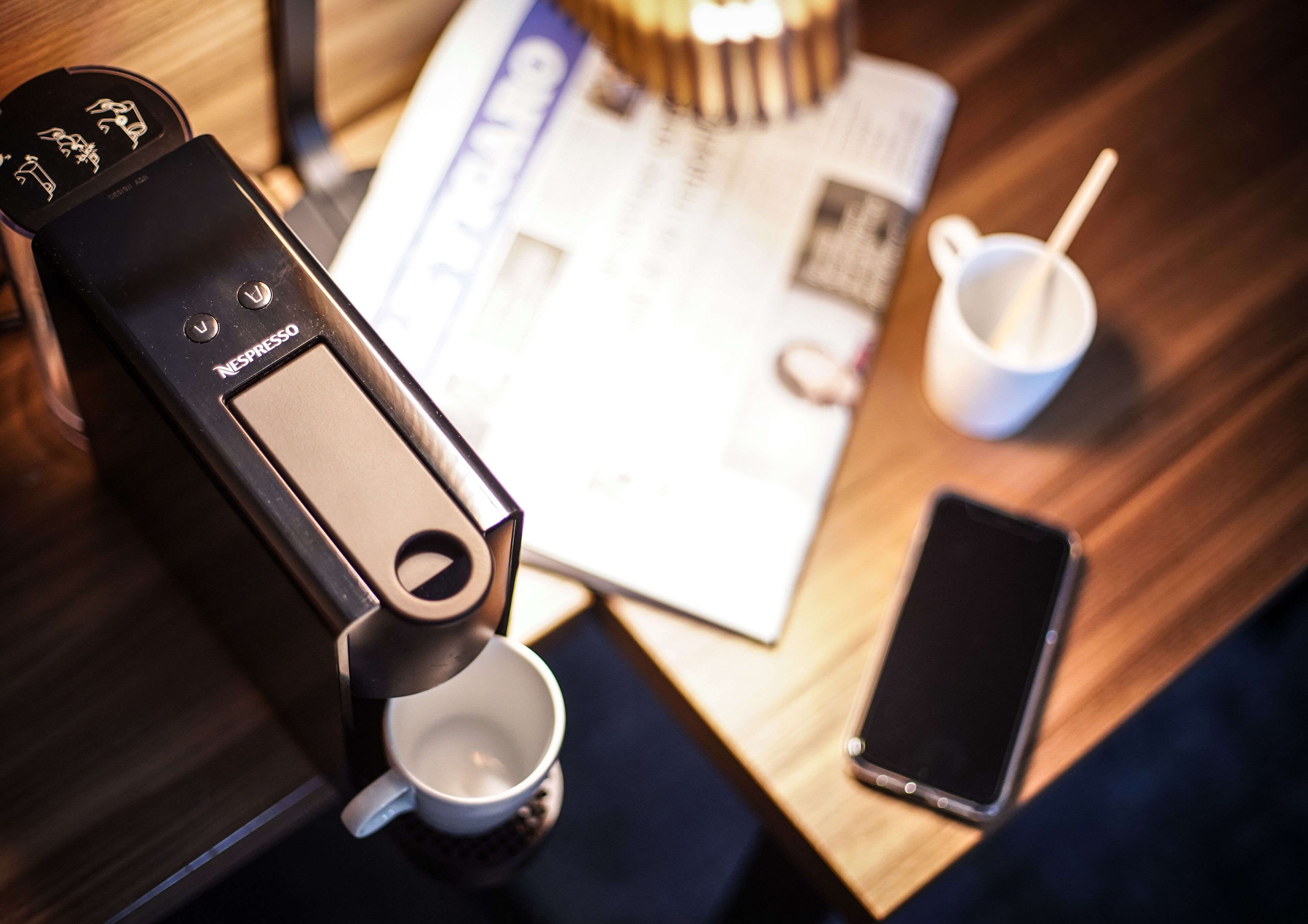 Une machine à café Nespresso, un téléphone intelligent, une tasse et un menu sur une table en bois.