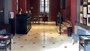 A spacious lobby with a marble floor, a reception desk, a dining area, and a staircase.