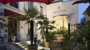 Un área de estar al aire libre con mesas y sillas, plantas en macetas y un edificio con un letrero que dice "le pavilion".